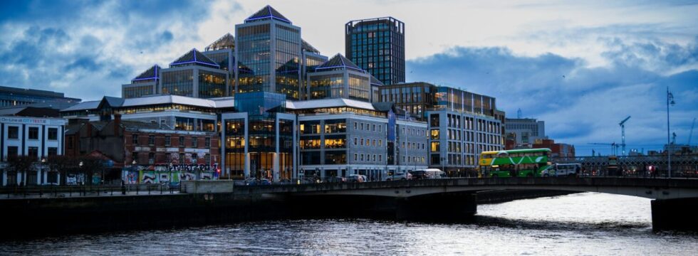 Bridging Loans Ireland - Riverside Office Buildings Bridging loans Ireland: modern office buildings beside a river under a cloudy sky